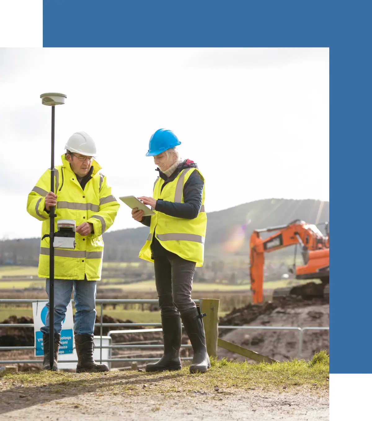 Two construction workers reviewing plans at a site with heavy machinery.